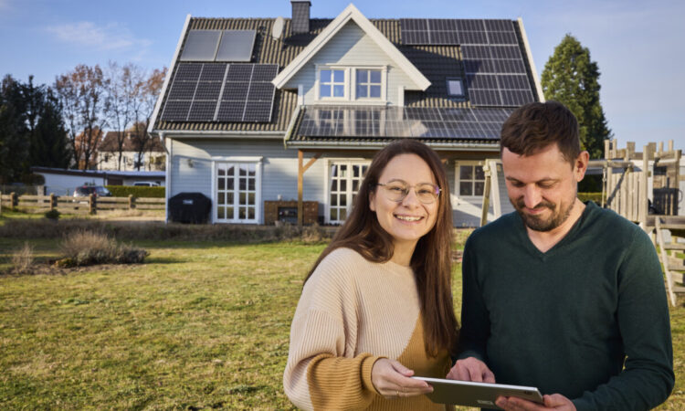 Paar vor einem Einfamilienhaus mit Photovoltaik-Anlage und iPad, die co2online/ co2online Produkte nutzen